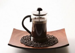French press and coffee beans on brown curved plate.